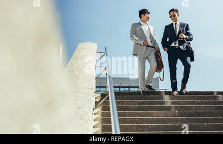 Two business partners walking together down stairs in the city. Korean business men walking down the steps and talking. Stock Photo