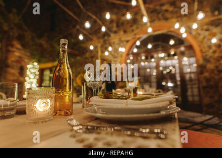 Table served for dinner party outdoors in evening with lights in background. Beautiful table setting for a big party in the night. Stock Photo