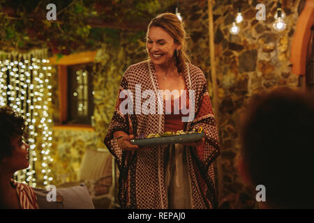 Smiling woman serving food to friends at dinner party. Party host serving food to friends during a party at night.