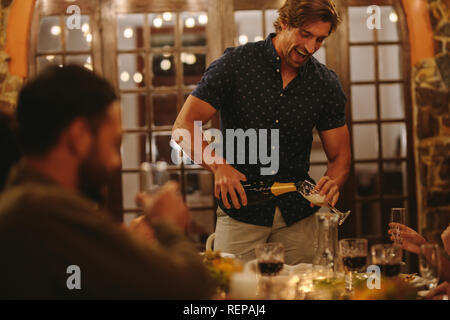 Man serving champagne to friends during party. Cheerful man pouring champagne into a flute during dinner party. Stock Photo