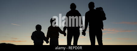 Silhouette of a family of five standing under the evening sky with their backs to the camera. Stock Photo