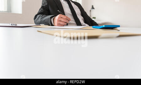Low angle view of business advisor or revisor sitting at his office desk surrounded with paperwork and documentation reviewing reports. Stock Photo