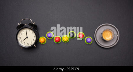 Coffee time. Alarm clock and espresso capsules, pods eco friendly, compostable on black color background,  top view Stock Photo
