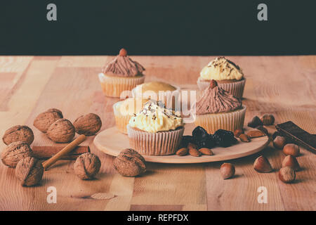 Homemade muffin cupcake with chocolate and vanilla cream, walnuts, hazelnuts and almonds on a wooden board- Image Stock Photo