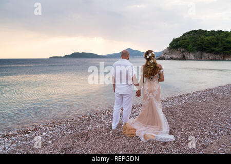 newlyweds stand on the beach and look at the sea hand in hand Stock Photo