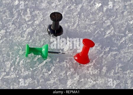Thumbtack in the colors red, black and green isolated on a snow background. Stock Photo