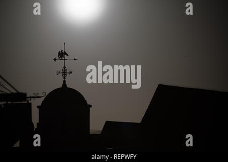 Black and white image of weather vane on top of cuppola roof with sun in the background Stock Photo