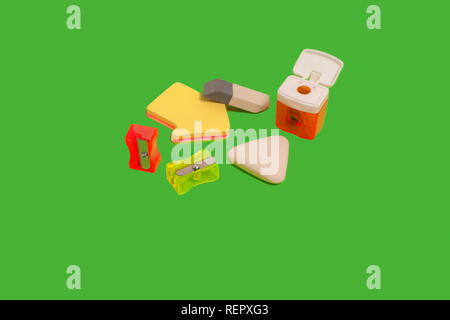 different erasers and sharpeners on a green surface Stock Photo
