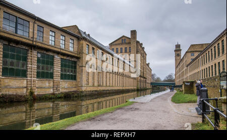 The Leeds Liverpool Canal at Saltaire,Yorkshire. Salts Mill buildings are on either side of the canal. A couple are reading a noticeboard. Stock Photo