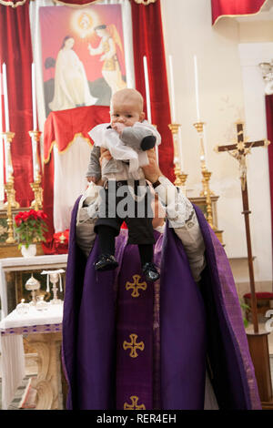 Priest holds a baby boy high up after his baptism in a catholic church Stock Photo