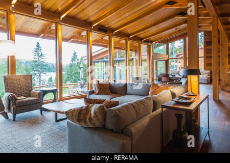 Grey upholstered sofas and high back armchair with wooden coffee table in living room area of great room with Ipe wood floor in cedar wood home Stock Photo