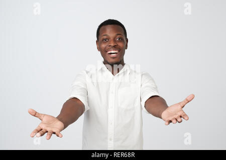 Cheerfull african man in white shirt, pulling hands towards camera, wanting to cuddle Stock Photo