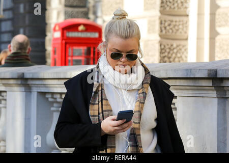 January 22, 2019 - London, United Kingdom - A woman is seen wrapped up with a scarf while looking at her mobile phone in Westminster on a sunny but cold day in the capital. According to the Met Office, temperatures are expected to drop to -4C as ''heavy snow downpours'' blanket the nation. (Credit Image: © Dinendra Haria/SOPA Images via ZUMA Wire) Stock Photo