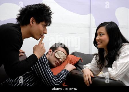Young man taking a quick power nap in the office is discovered by his colleagues Stock Photo