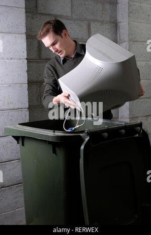 Man disposing of obsolete computer technology in a wheelie bin Stock Photo