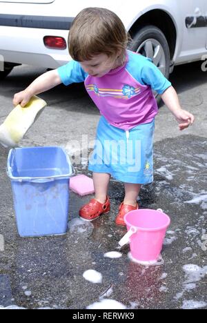 Two year old girl having fun helping to wash the family car Stock Photo