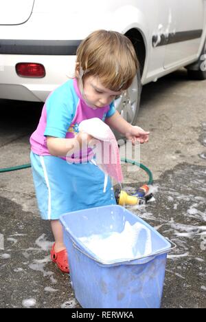 Two year old girl having fun helping to wash the family car Stock Photo