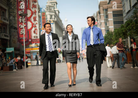 Three business colleagues walking down a busy street while talking. Stock Photo