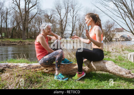 Senior and young woman resting on log after sport Stock Photo