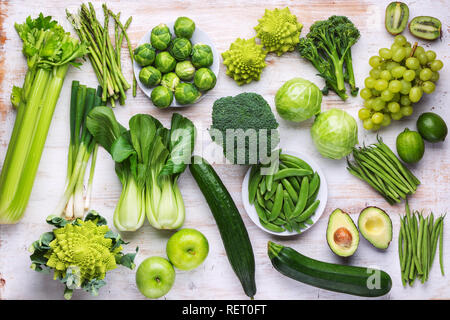 Healthy eating vegan concept. Green vegetables fruits on white table broccoli sprouts peas avocado courgette beans bok choy celery apple grapes, top v Stock Photo