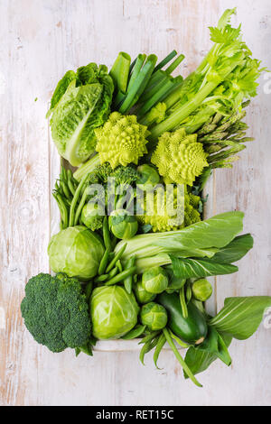 Healthy eating vegan concept. Green vegetables on white table broccoli sprouts peas avocado courgette beans bok choy celery in wooden box, top view, s