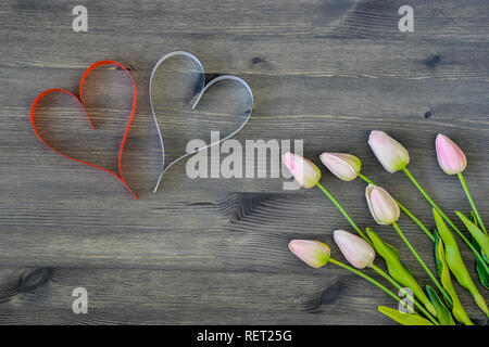 Two hearts of red and white with tulips in a soft pink shade on a wooden background. Romantic card concept. The view from the top. Flat lay. Stock Photo