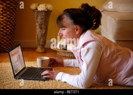 Woman, 45 years old, surfing the internet with a laptop in her flat Stock Photo