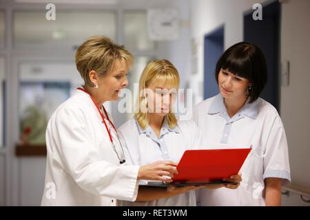 Female doctor talking to two nurses in a hospital ward corridor Stock Photo