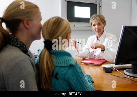 A female doctor talking to a mother and her daughter in a hospital doctor's office