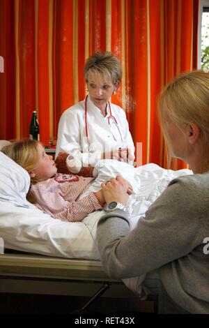 Doctor talking to a young patient, seven years old, and her mother at the bedside in a hospital Stock Photo