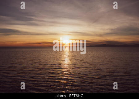 Sunset over the sea with mountains in the background Stock Photo