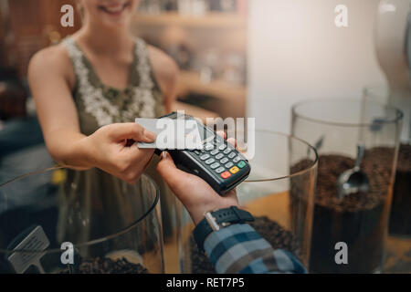Hand of customer paying with contactless credit card with NFC technology. Waiter with a credit card reader machine and with female smiling holding cre Stock Photo