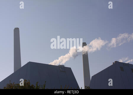 Modern power plant with chimney and column of smoke backlit against a blue sky with copy space Stock Photo
