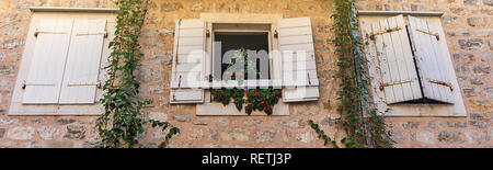 Old windows with shutters and pots with flowers in the stone wall Stock Photo