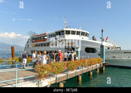 GARDONE RIVIERA, ITALY - SEPTEMBER 2018: People waiting on the ferry landing stage in Gardone Riviera on Lake Garda. In the background, a passenger fe Stock Photo