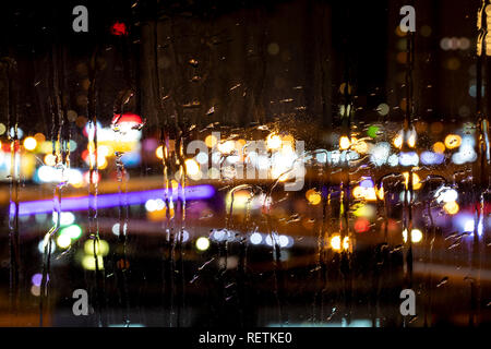 Rain drops on window with road light bokeh. City life in night in rain Stock Photo