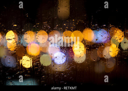 Rain drops on window with road light bokeh. City life in night in rain Stock Photo