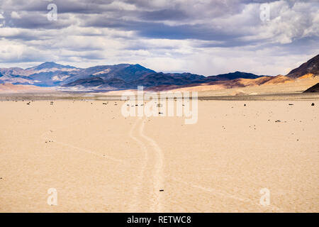 Moving rocks and their tracks at the Racetrack Playa; mountains and clouds scenery in the background; Death Valley National Park, California Stock Photo