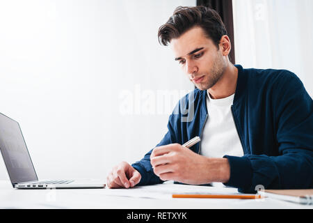 Young man designer working at modern loft studio sitting at table while working on laptop. Portrait of manager in office using notepad and computer Stock Photo