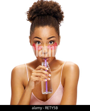 Young girl with pink eye patches on her face and drinks clean water. Photo of african american girl isolated on white background. Youth and Beauty Stock Photo