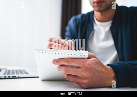 Young businessman sits by table and make business plan using notepad and pen. Coworker man working in office space Stock Photo