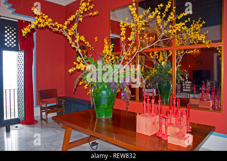 Big green vase with yellow flowers and red candles on the table, mirrors on the wall, marvel floor, red interior Stock Photo