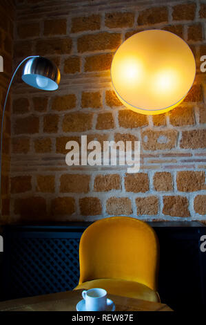 Yellow velvet chair in the corner, round lamp on the brick wall Stock Photo