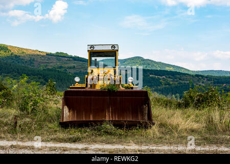 Old abandoned broken yellow excavator, near the lake Zavoj, on an Old mountain. Rusty and with the damaged tires resisted the teeth of time. Stock Photo