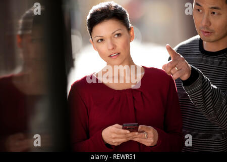Man points out directions to a young woman holding her phone. Stock Photo