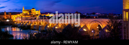 Panorama of ancient stone Roman bridge illuminated in night time with glowing Moorish Mosque Cathedral (Mezquita) on background in Cordoba, Spain Stock Photo