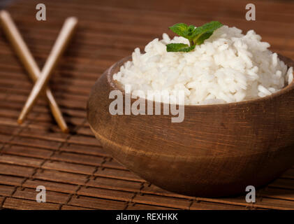 Cooked white rice in wooden bowl with chopsticks on a wood brown bamboo background. Stock Photo