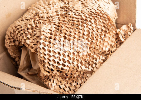 A bunched recyclable perforated brown paper filler on top of an opened box package. Stock Photo