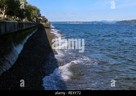 Sea wall at Alki Beach in West Seattle Washington with view of Cascade Mountains in the distance on a sunny day with clear blue sky Stock Photo