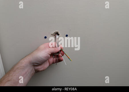hand holding Control wire for thermsotat used with a HVAC unit, coming out of wall during installation Stock Photo